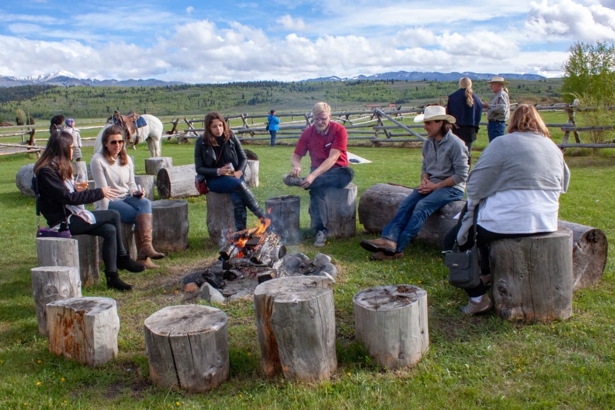Patrons enjoying wine and a campfire at a ranch.