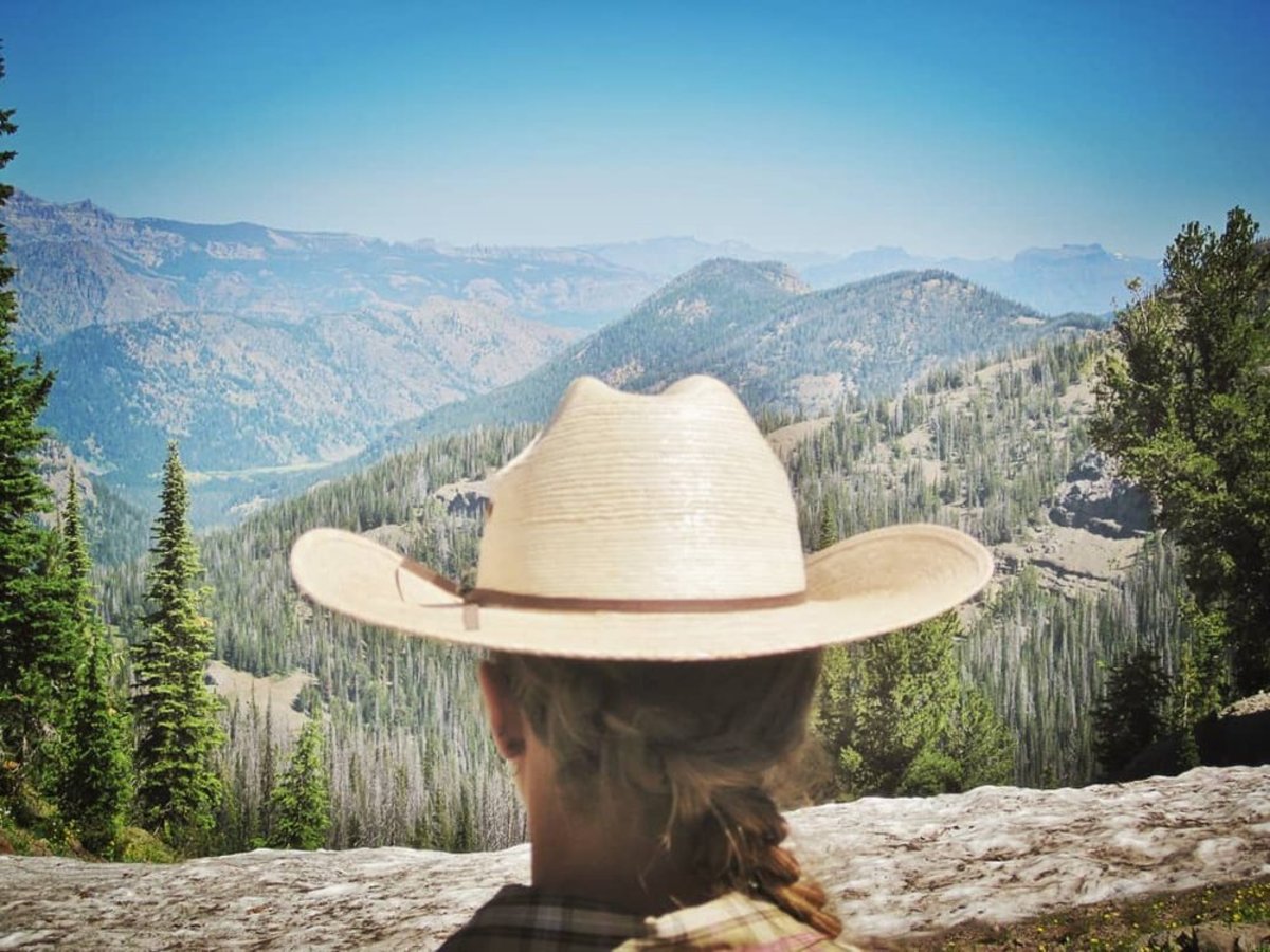 A woman with a hat stands before a mountain range in the Shoshone National Forest which has numerous campgrounds