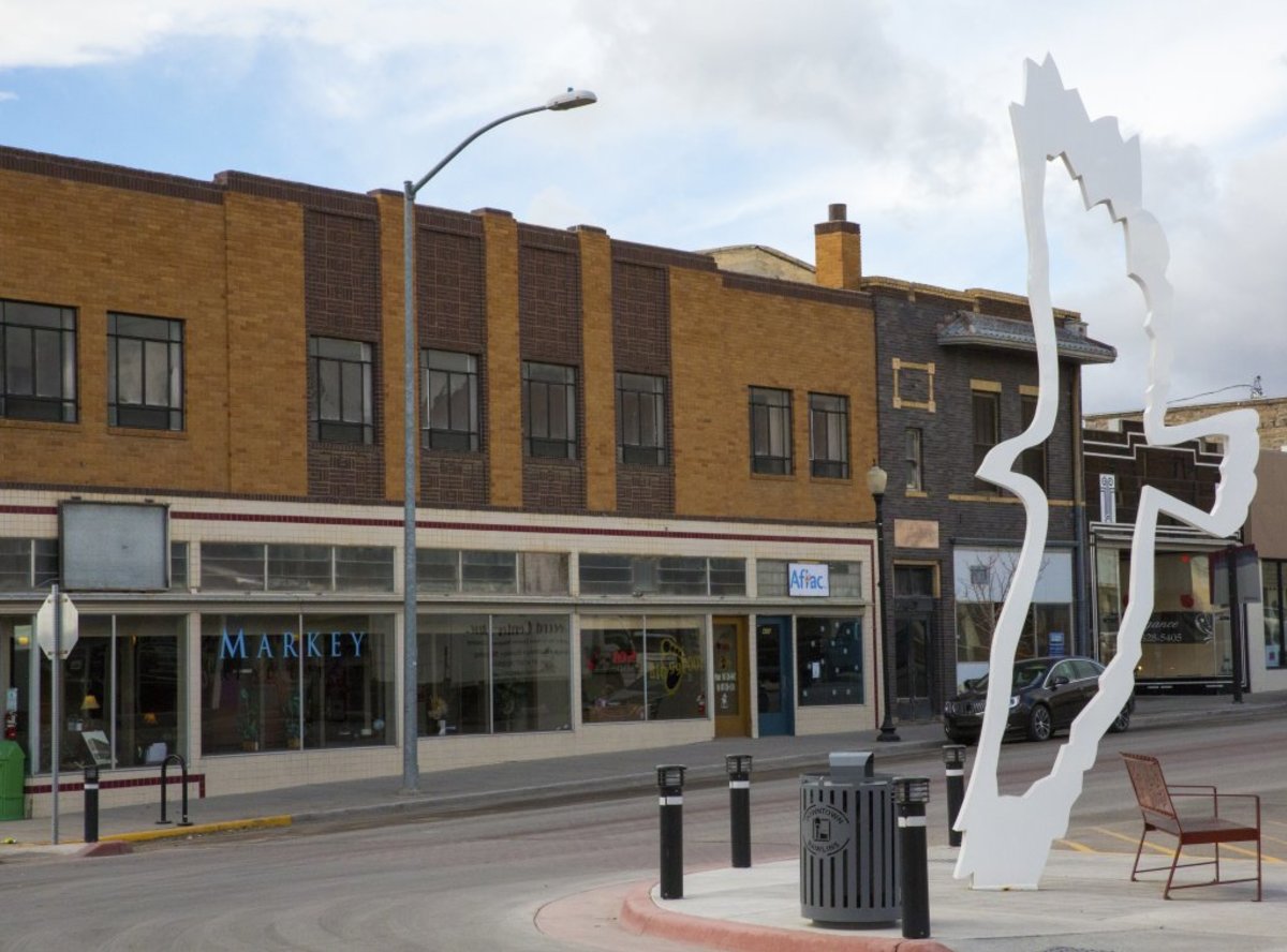 A view of the main street in Rollins, Wyoming, where a white statue of the outline of a bird soaring hangs before the building that reads, "Markey" with "Aflac" right next door. 