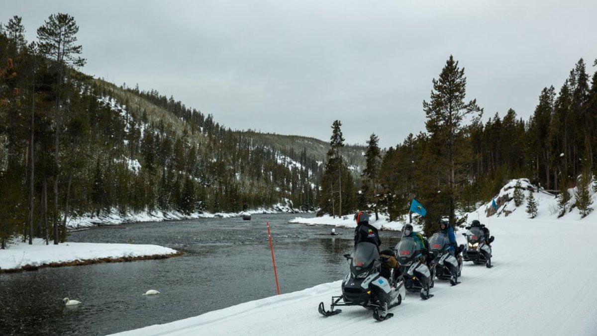 A group of snowmobilers along a lake in Yellowstone National Park during the winter season.
