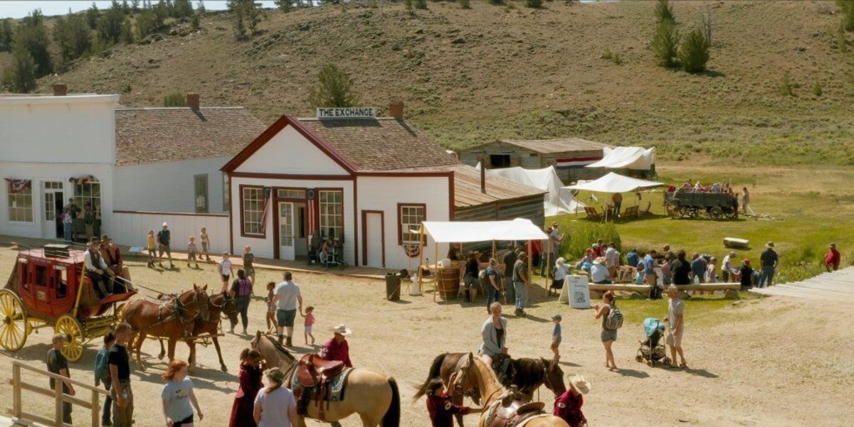A row of historic buildings lining a dirt road filled with horses, people and a horse-drawn carriage at the ghost town of South Pass City.