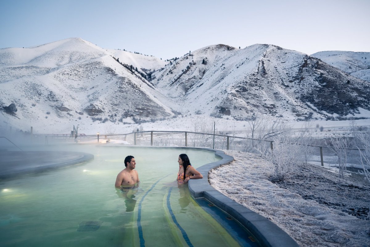 Steam rising from a natural hot spring with people soaking surrounded by snowy landscapes at Astoria Hot Springs Park in Wyoming.