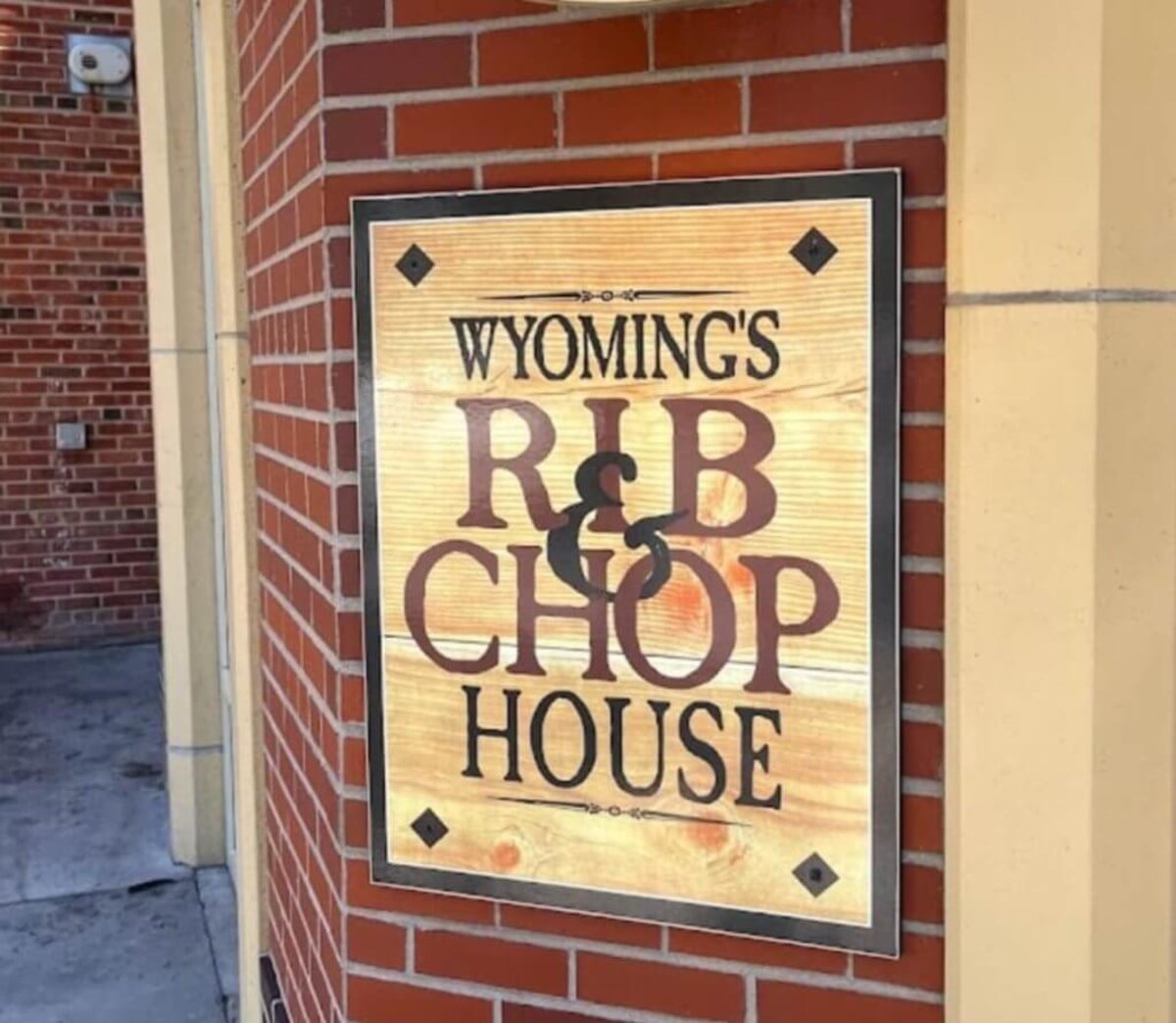 An up close view of a wooden sign on a brick building that reads Wyoming's Rib & Chop House.