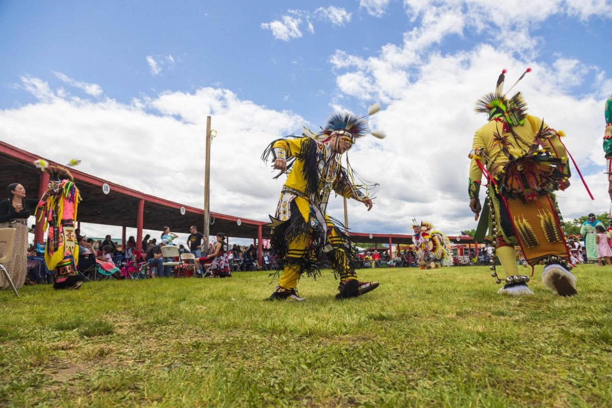 A group of men wearing traditional clothing and performing in a field surrounded by a crowd at the Annual Eastern Shoshone Indian Days Powwow.