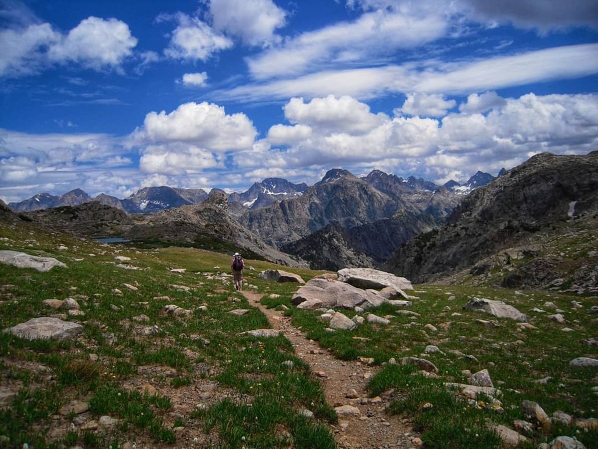 Man hiking across grass towards mountain range in one of Wyoming's national parks during the summer.