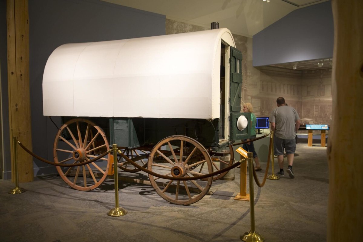 People viewing an exhibit of a covered wagon inside the Buffalo Bill Center of the West.