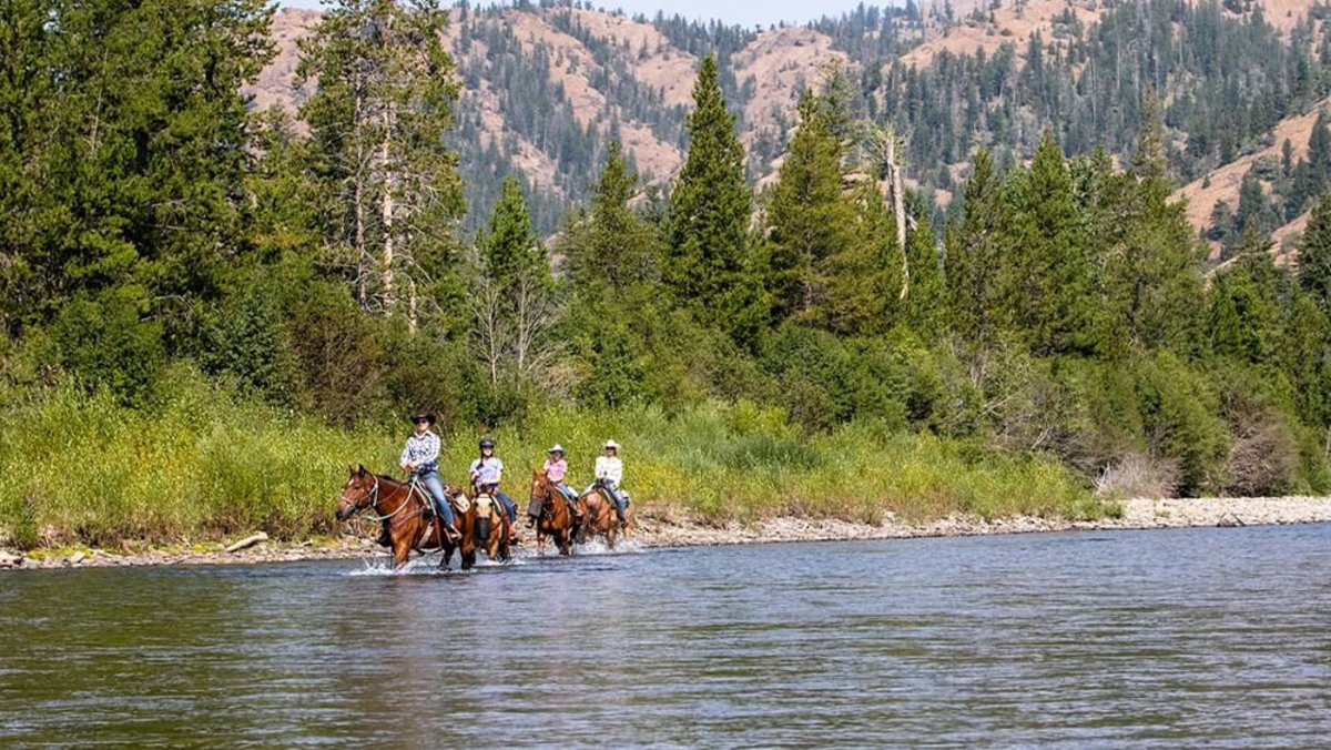 Horseback riders on river side at a dude ranch in Wyoming during the summertime.