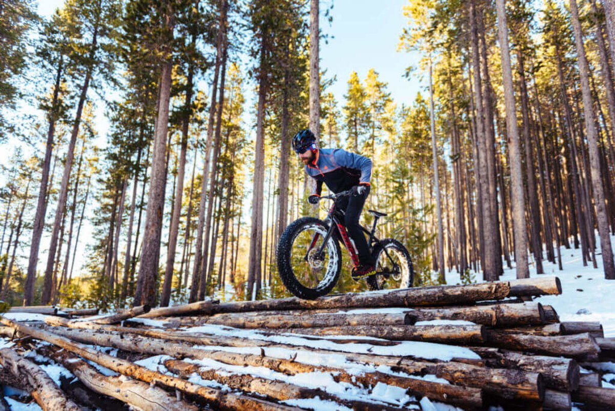 A mountain biker traversing over some logs in the snowy forest, one of the many things to do on Casper Mountain.