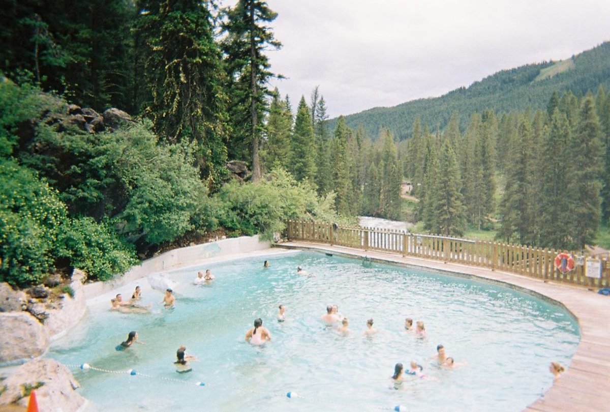 Several people soaking in the pool at Granite Hot Springs, surrounded by a forest of trees and a forested hill in the distance.