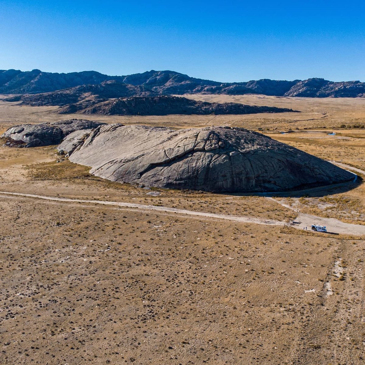 A distant view of rugged Independence Rock beneath a bright blue sky.