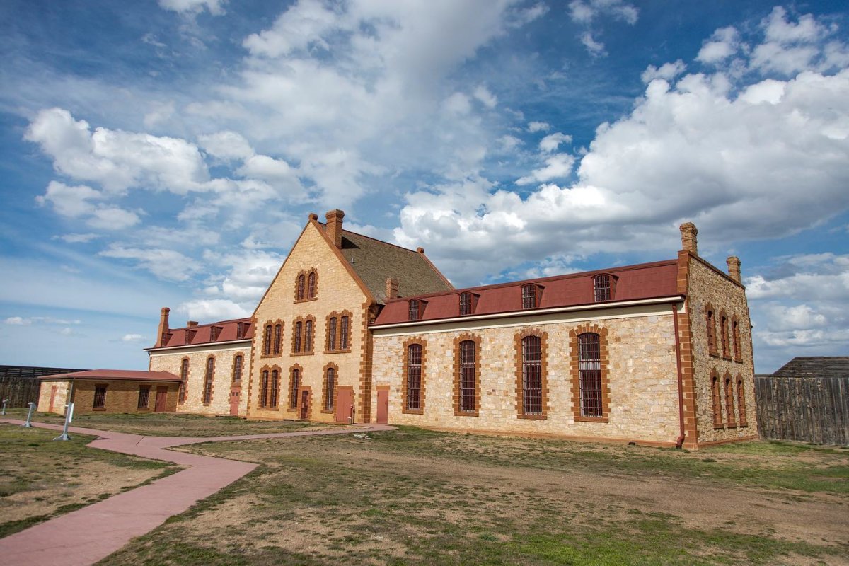 The stone exterior of the historic Wyoming Frontier Prison with arched windows and red roof accents under a partly cloudy sky.