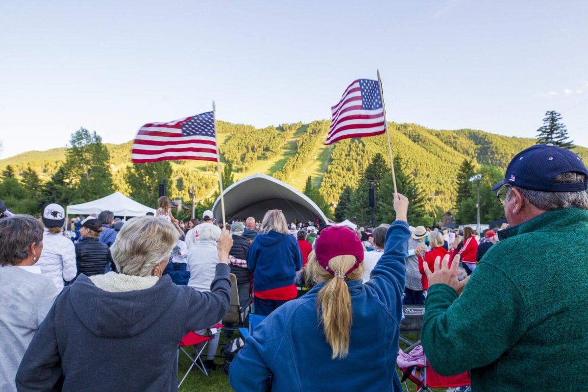 A crowd gathers, waving American flags, at an outdoor event.