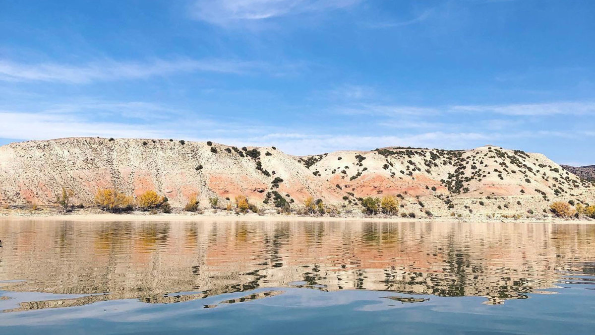 A large, scenic lake in front of rolling white and red hills.