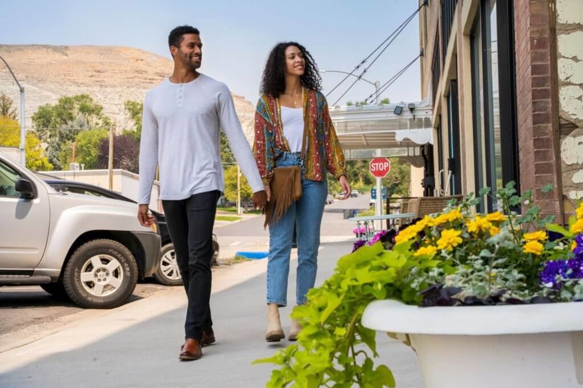 A couple holds hands as they walk towards a pot of vibrant flowers on the main street in Green River, a town in Wyoming, where a mountain towers in the distance.