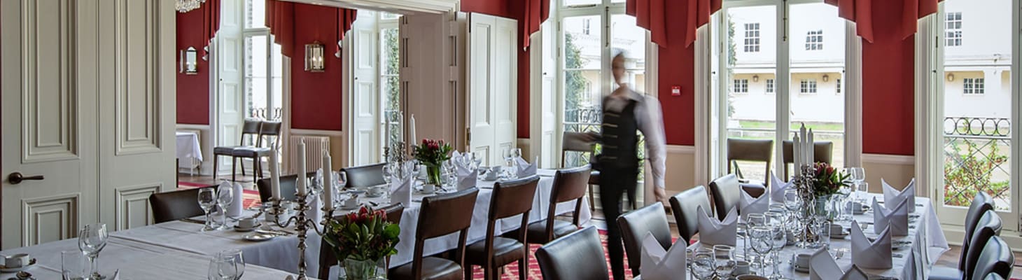 Dressed banqueting tables in a cream and red dining room with floor to ceiling windows, perfect for private dining.