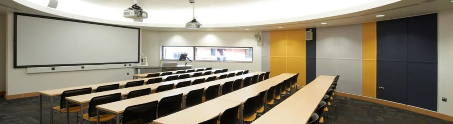 Classroom with attractive suspended round celling with lights, wooden desks, yellow walls and chairs for small meetings.