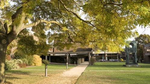 Autumnal photo of lawn with pathway leading into a building with a view of a sculpture.