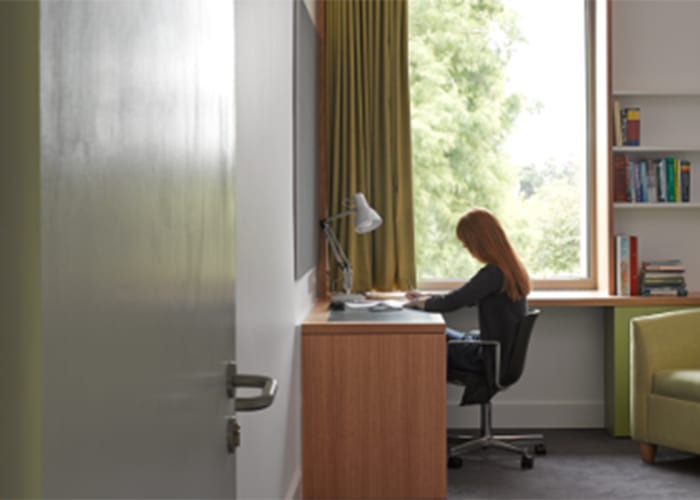 A guest sitting at a desk in a single ensuite bedroom at Girton College, ideal accommodation for conference delegates.