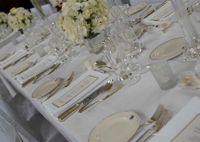 A dining table set with menus, silver crockery, and fresh cream flowers, a wonderful setting for a gala dinner.