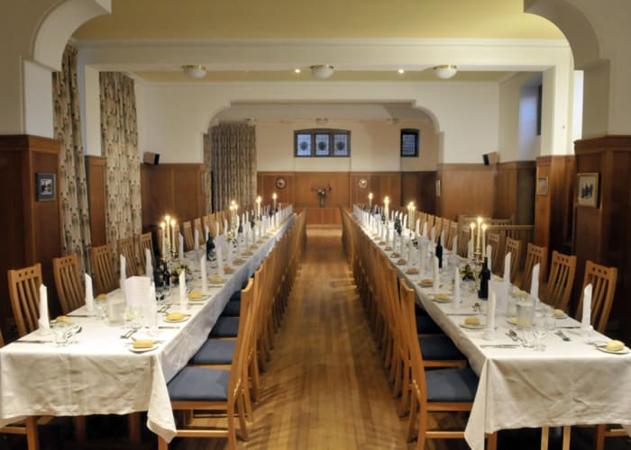 Traditional function room with wood flooring and wall paneling, finished with cream decor. Tables covered with cream cloths and set for formal dining with wooden chairs