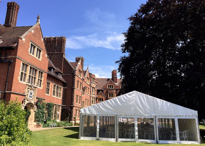 Large marquee set up on the sun trap lawn at Trinity Hall, ready for a summer garden party, with shading from the trees.