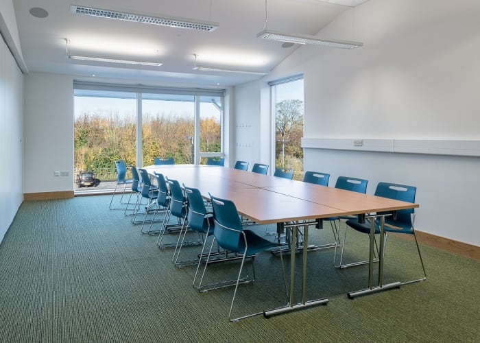 A modern meeting room filled with natural daylight set with a large table and chairs, suitable for day meetings.