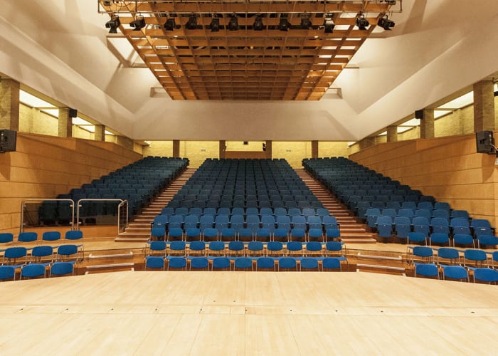 Very large modern, open and bright lecture theatre with rows of blue chairs and a raised stage area to present from. Ideally for large conferences and events.