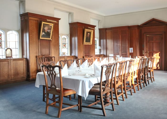 A small dining table is set for a private dinner in the Old Library, a wooden panelled room with stained glass windows.