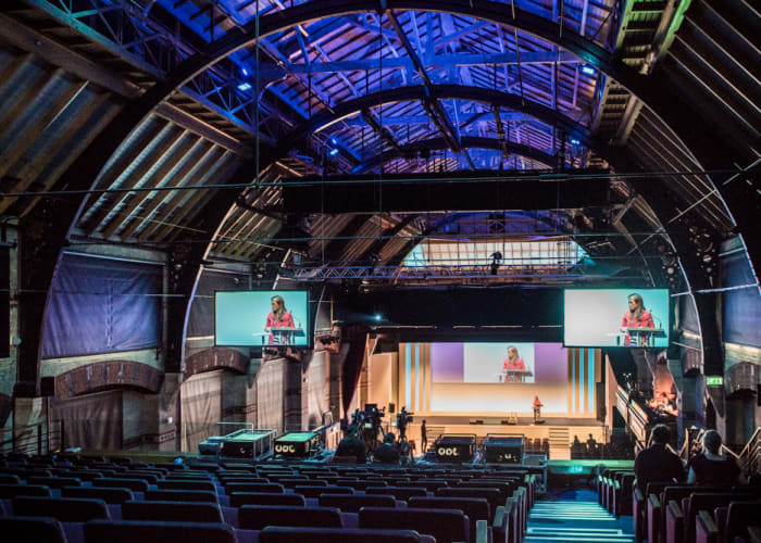 Multiple screen set up at the Corn Exchange in the auditorium with plenty of tiered seating with a detailed arch ceiling.