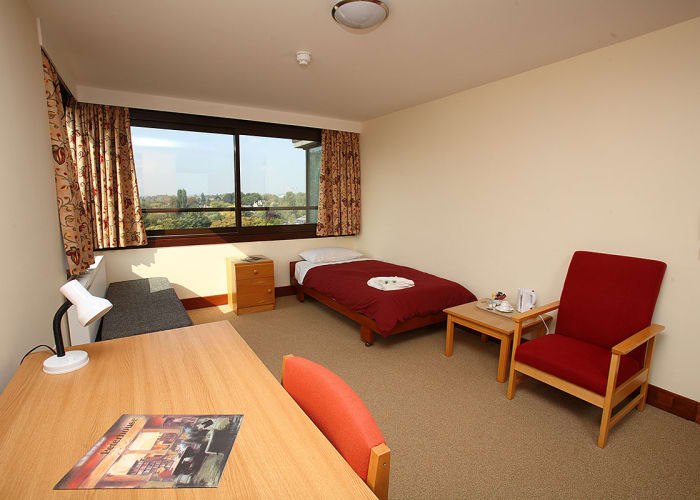 Large bright spacious single bedroom with bedside cabinet, a desk with chair and seating area. Room also offers a large wide window that gives lots of natural daylight.