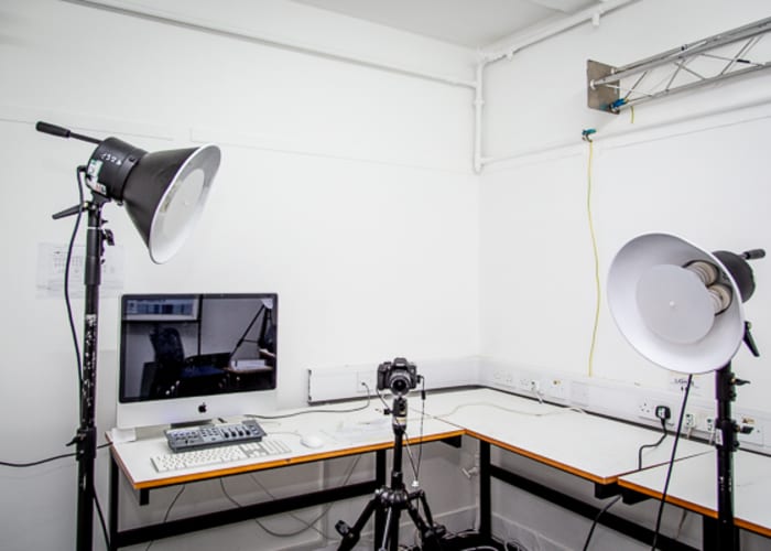 A small animation suite with white walls, camera on tripod, computer and two large lamps