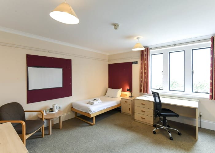 A single en suite bedroom in Ann's Court, Selwyn College, the room is complete with bed, desk, chair and armchair.