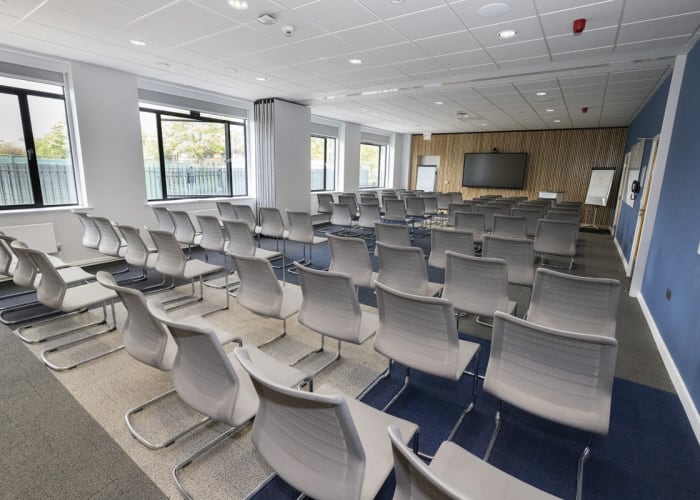 A flexible meeting room set theatre style with rows of chairs and a aisle in the middle of the room. Fully equipped with AV equipment.