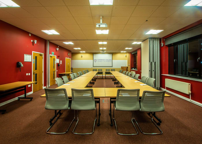 Long room with red decor, hollow boardroom style set up with a screen at the top of the room. Multi-functional meeting space in Cambridge