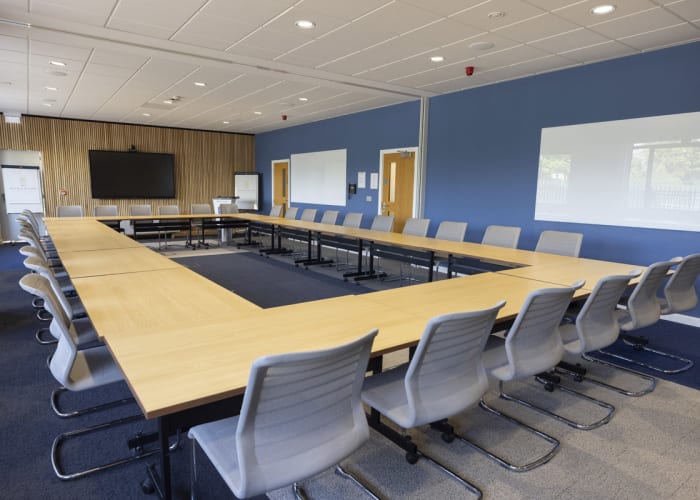 A spacious room with hollow boardroom style set up with a screen at the top of the room. Multi-functional meeting space in Cambridge