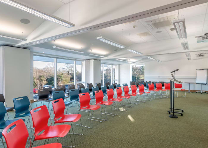 A bright and modern conference room set with rows of chairs, floor to ceiling windows let in ample day light.