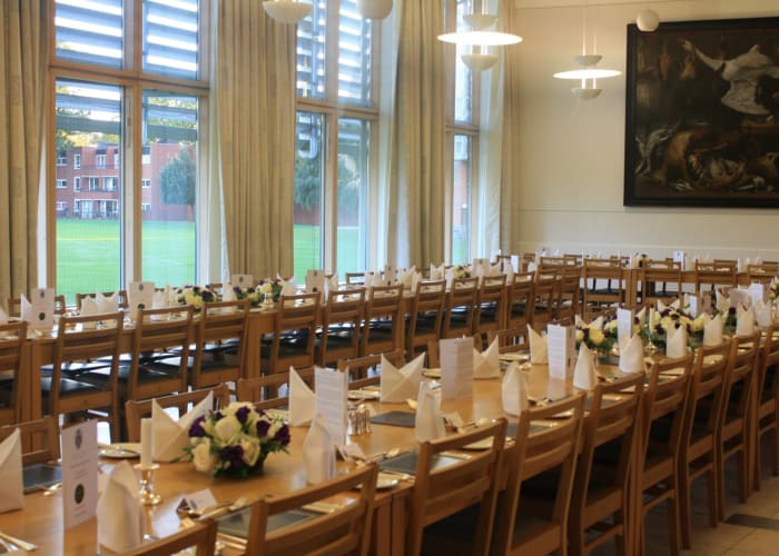 Dining Hall at Hughes Hall set for a private dinner, the table is set with fresh flowers, menus and napkins.