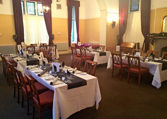 Traditional room, long tables set for a Christmas meal, tall windows with dark red curtains and cream walls