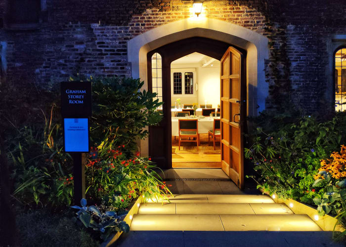 Photo of the exterior of the Graham Storey Room entrance at night with outdoor step lights showing off the flower beds.