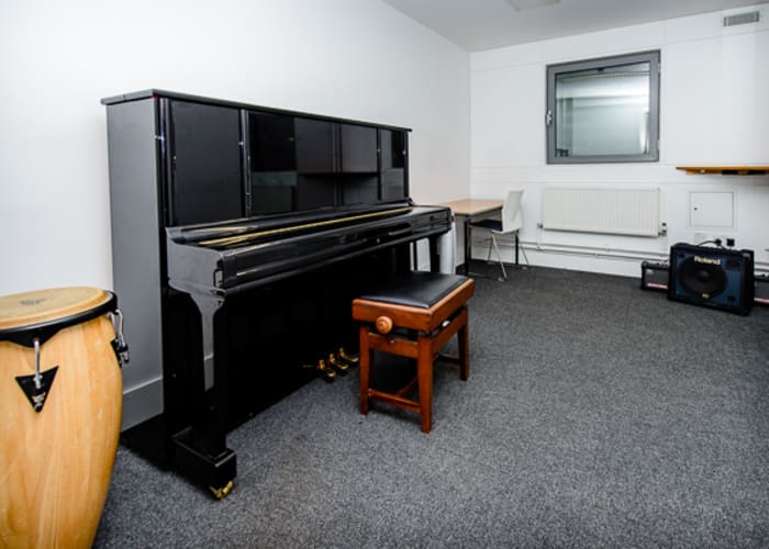 A small music room with white walls, piano, drum and various other musical instruments for room hire