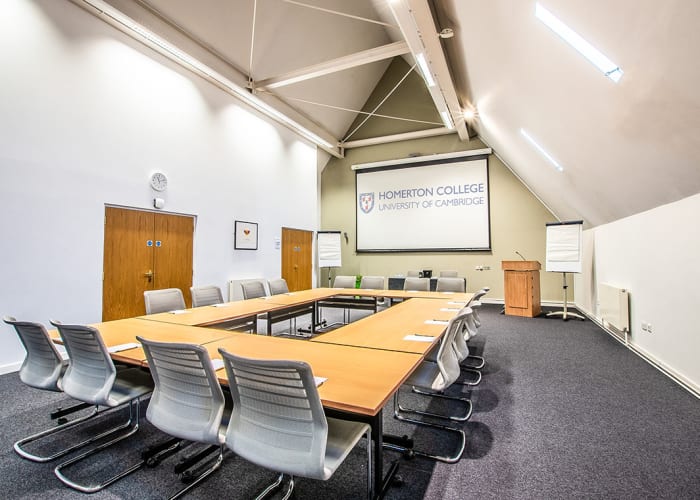 Modern tall ceiling meeting room with a slanted angled ceiling, bright space with one large hollow boardroom with  chairs around the table and a screen at the front of the room.