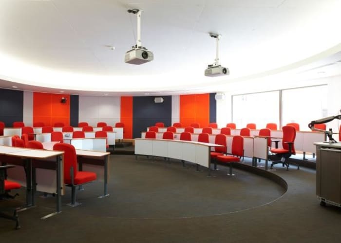 A round shaped meeting room with navy and red striped wall color, long white desks and red chairs on a tiered floor.