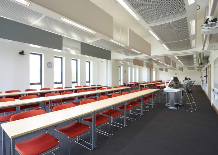 A bright long large meeting room with long desks and red chairs.
