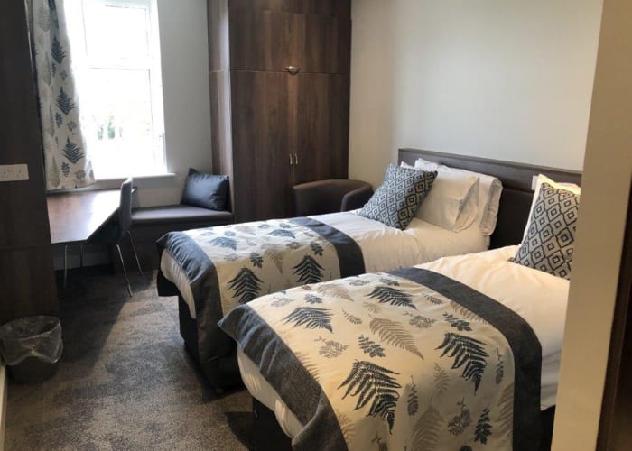Venue with accommodation, North Wing bedroom decorated in a contemporary style with lots of natural daylight. Two single beds with a throw and additional cushions on each bed, desk, chair and wardrobe