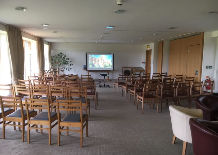 A bright meeting room with rows of chairs and a screen at the front, ideal for presentations.
