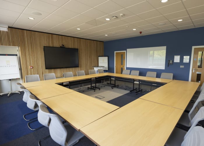 Modern event space in Cambridge, Bright room with large windows, set up in a hollow boardroom style and refreshments available to the side of the room and fully equipped with AV equipment.