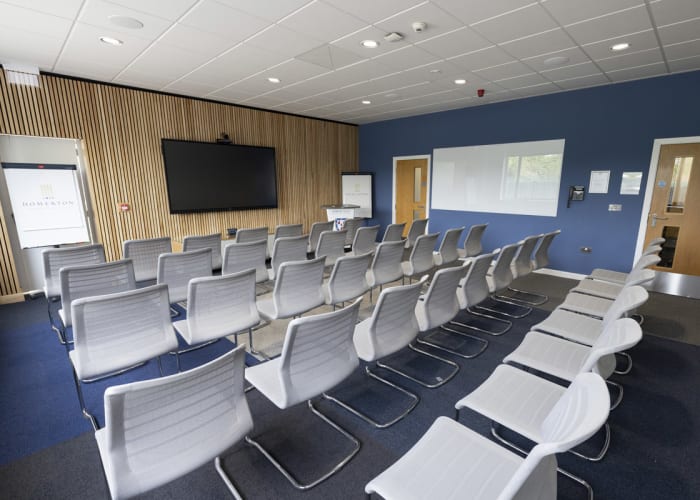 Modern event space in Cambridge, Bright room with large windows, set up in a theatre style with rows of chairs and fully equipped with AV equipment.