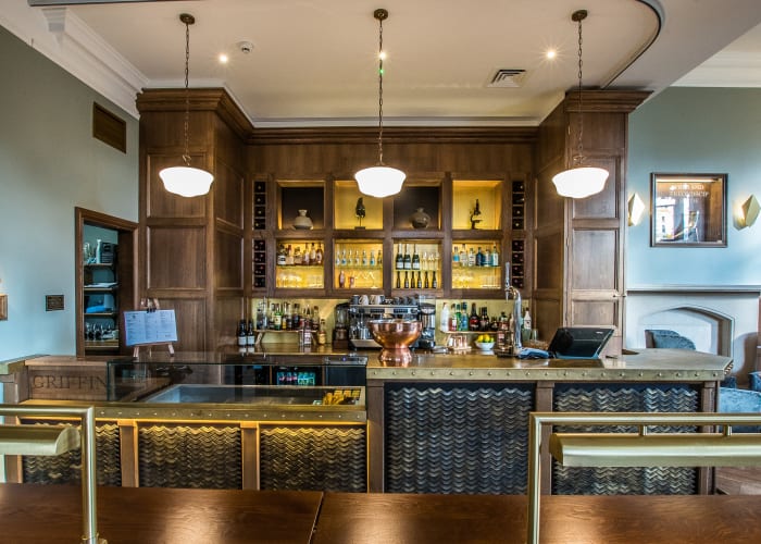 Stylish bar area with a mix of blue and dark wood paneling on the walls and chrome features around the room, 3 low hangin lights, modern yet also traditional area. Lots of different bottles of drinks on display so you can see what is available to purchase