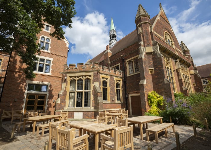 Outdoor numerous individual wood chairs and tables with a impressive backdrop of the traditional Homerton College building with bright seasonal trees and bushes surrounding the area
