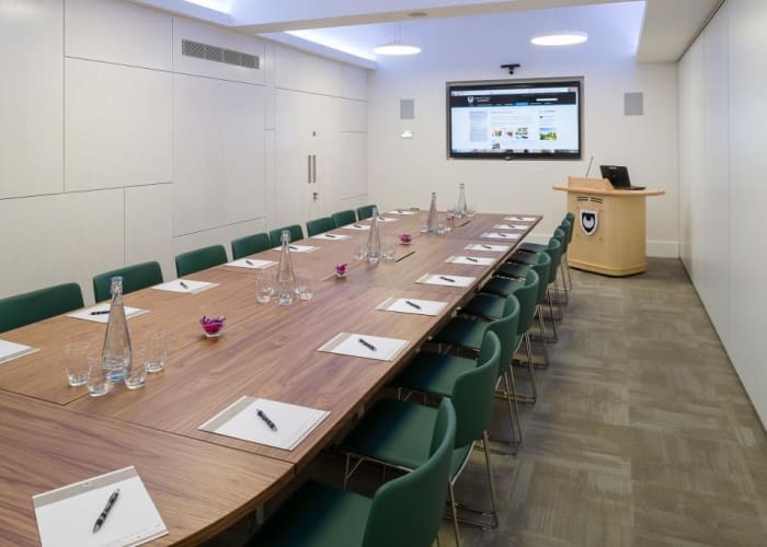 A large boardroom table and chairs, equipped with an AV system, in the breakout meeting room in WYNG Gardens, Cambridge.